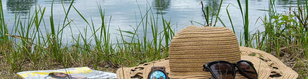 Hut und Sonnenbrille liegen im Gras vor See